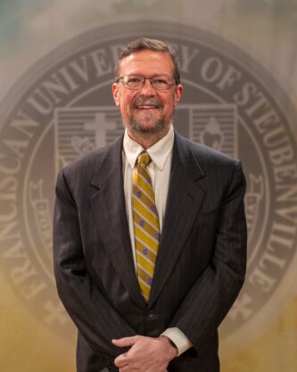 Faculty portrait of Dr. Michael Sirilla standing in front of the Franciscan University of Steubenville seal.