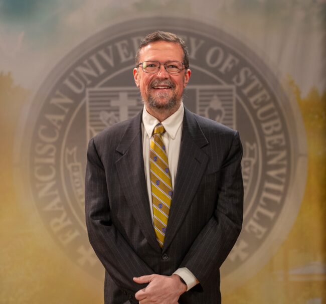 Dr. Michael Sirilla_Faculty Portrait_Spring2026_-2823 Faculty portrait of Dr. Michael Sirilla standing in front of the Franciscan University of Steubenville seal.