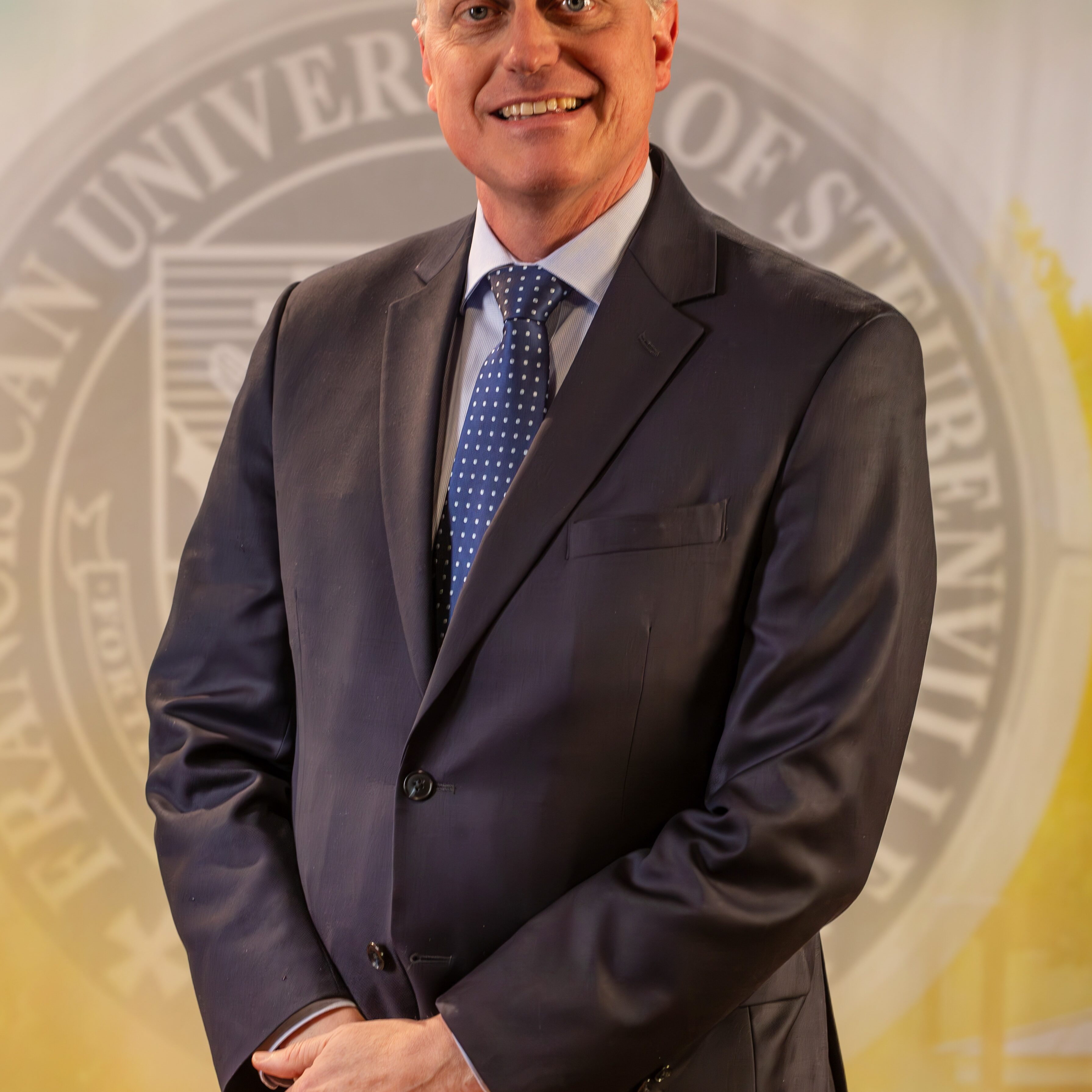 To Web – Dr. John Bergsma FEB2025 –4 Dr. John Bergsma standing in front of the Franciscan University of Steubenville seal.