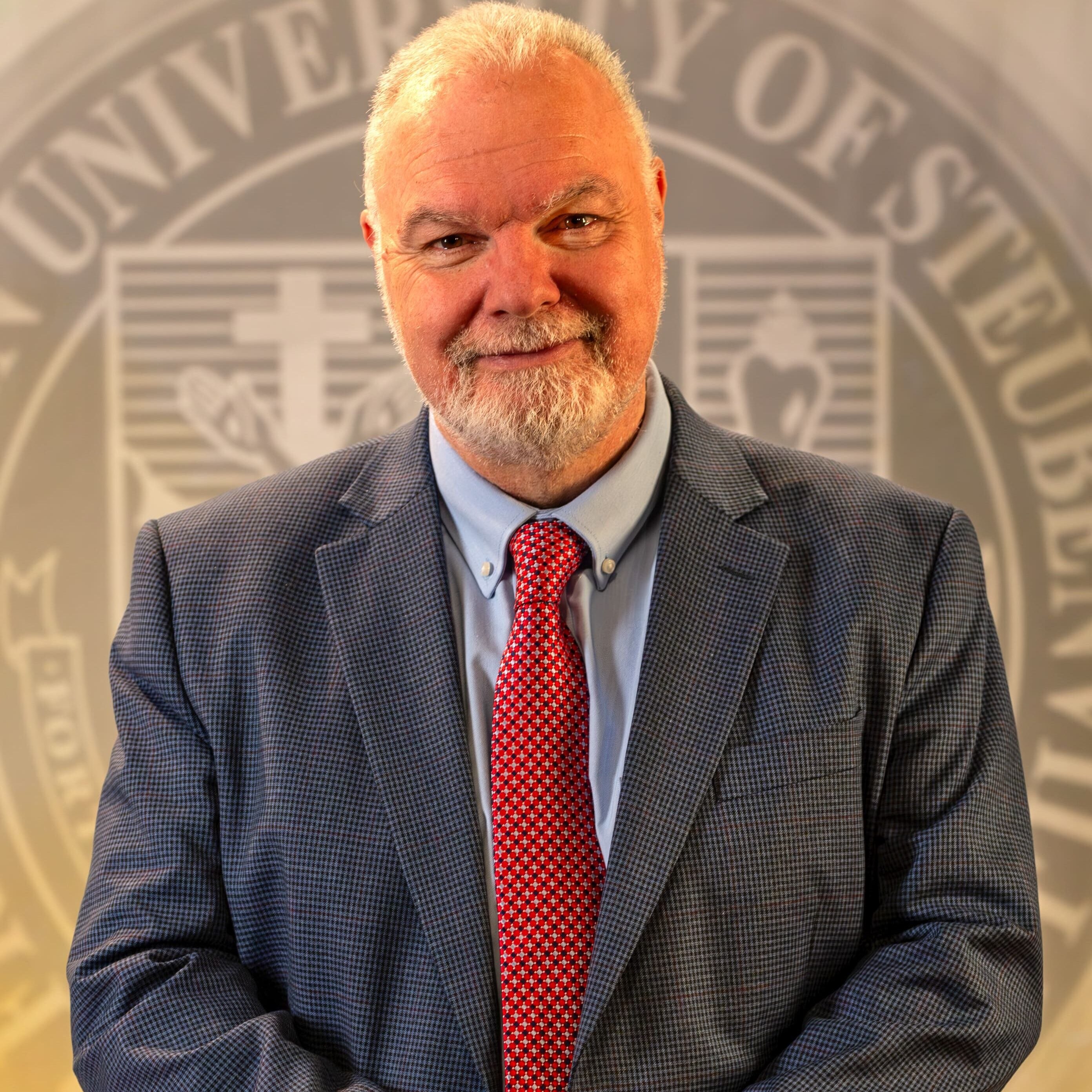 To Web – Dr. Petroc Willey FEB2025 –6 Dr. Petroc Willey standing in front of a university seal.