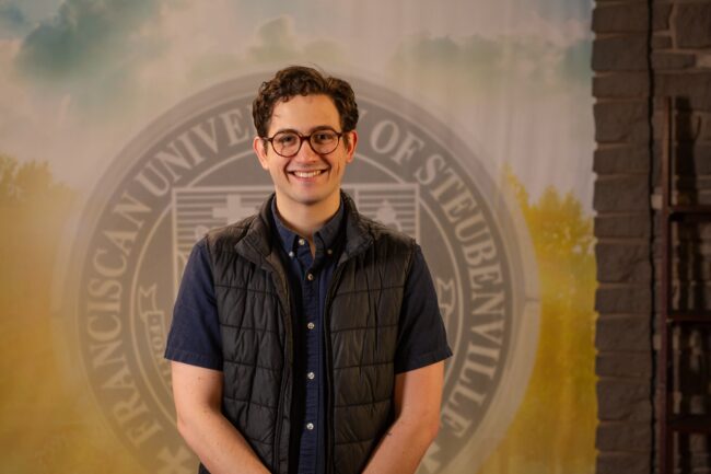 Nick Riccardi standing in front of a college seal.